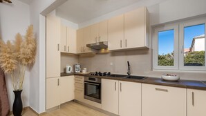 A modern kitchen with light-colored cabinets, a stainless steel oven, and a window with a view of greenery. - Nice Home in Pag With Wifi and 2 Bedrooms (Pag)