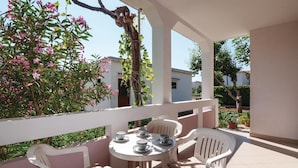An outdoor patio with a round table and four white chairs, surrounded by a white railing and pink walls. - Nice Home in Pag With Wifi and 2 Bedrooms (Pag)