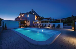Ein zweistöckiges Haus mit Swimmingpool, Sitzgelegenheit im Freien und einer gut beleuchteten Terrasse.