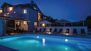 Une piscine entourée de chaises longues et d’un parasol, le tout bordé par un bâtiment doté de nombreuses fenêtres et d’une antenne parabolique.