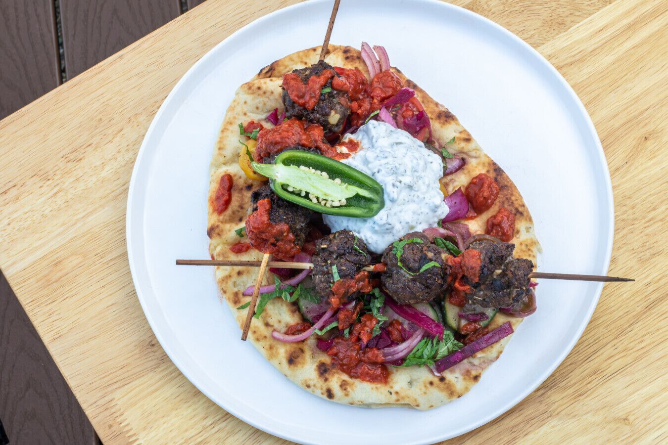 Un piatto di cibo con kebab, piadina e un cucchiaio di salsa su un tavolo di legno.