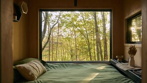 Ein Schlafzimmer mit einem großen Fenster und Blick auf einen Wald.