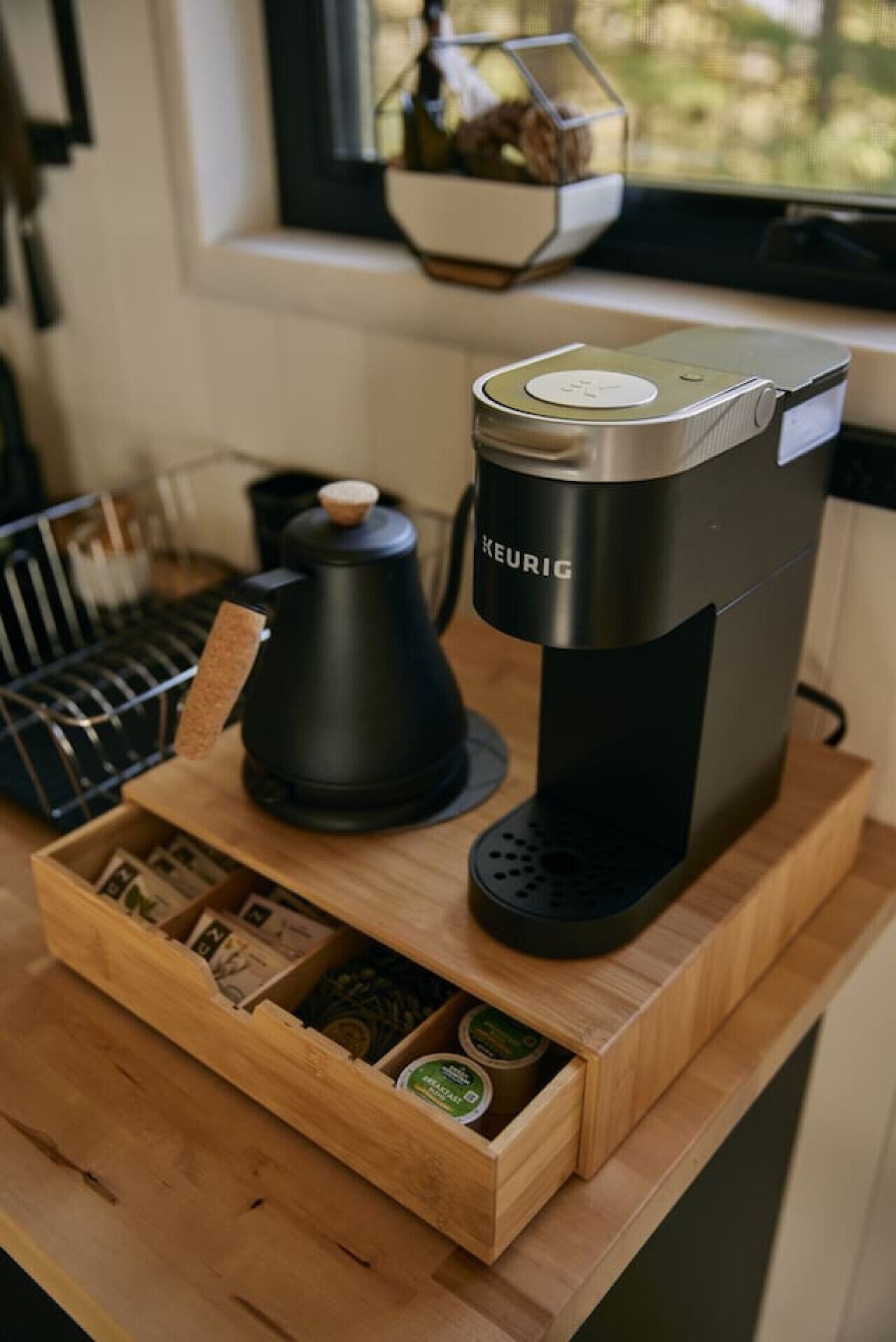 Una cafetera Keurig sobre una mesa de madera con un cajón que contiene cápsulas de café.