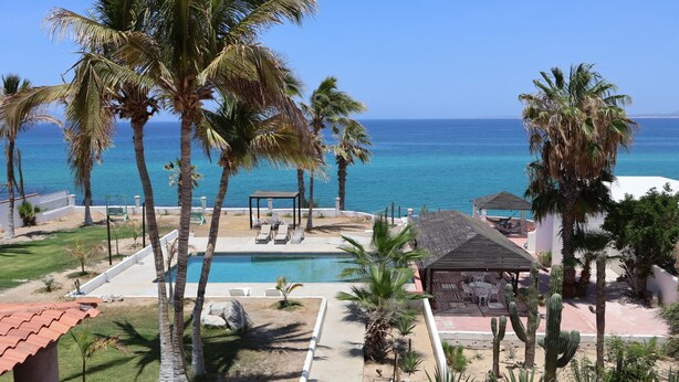 A pool area with lounge chairs, palm trees, and a view of the ocean. - Vista al Mar (El Sargento)