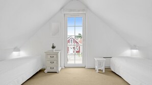 A white, triangular attic bedroom with a large window, a small white table, and two white beds. - Gorgeous home in Brenderup Fyn (Brenderup Fyn)