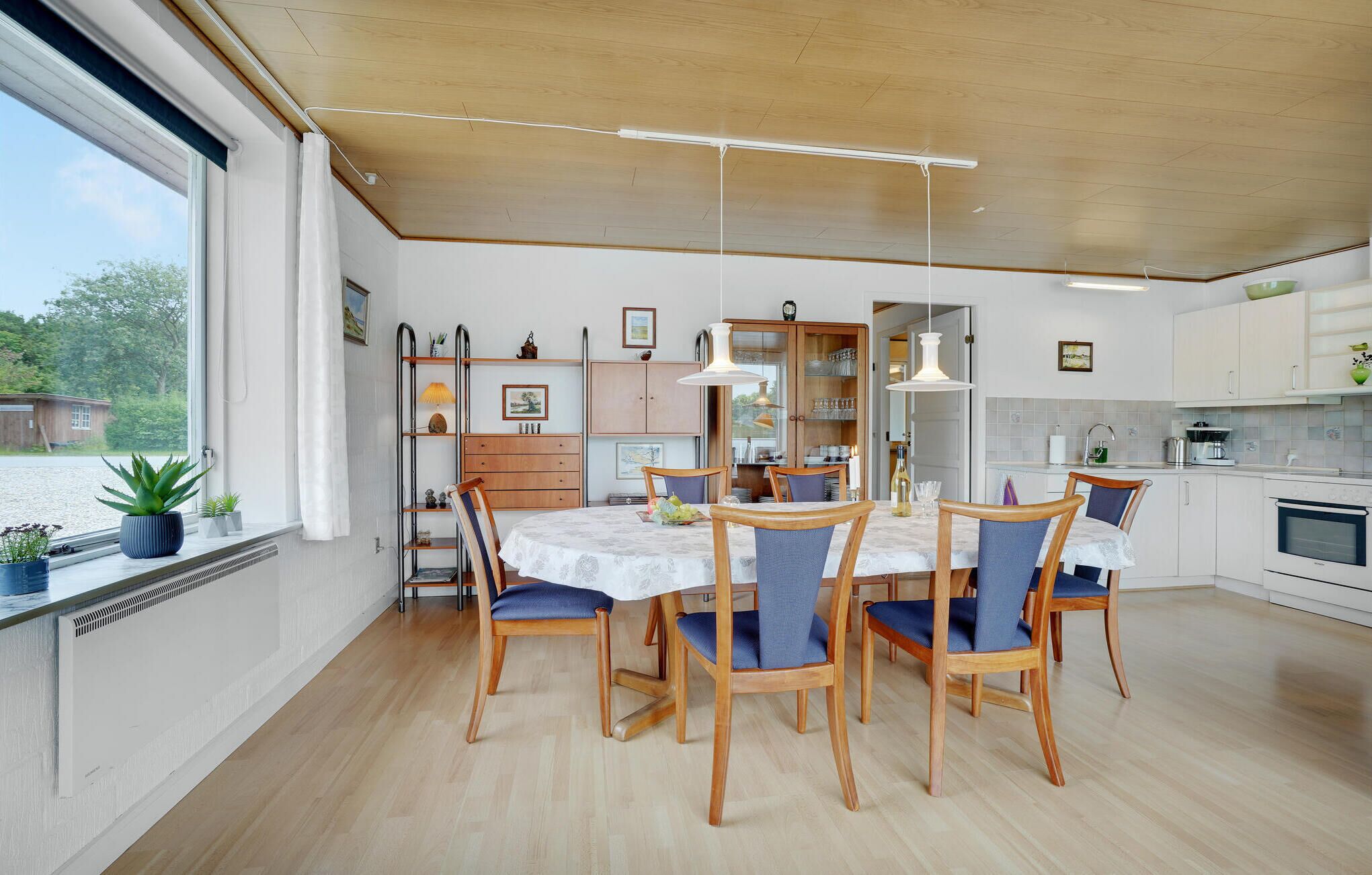 Una cucina moderna con mobili in legno, un tavolo da pranzo con sedie e vista su un corpo d'acqua attraverso ampie finestre.