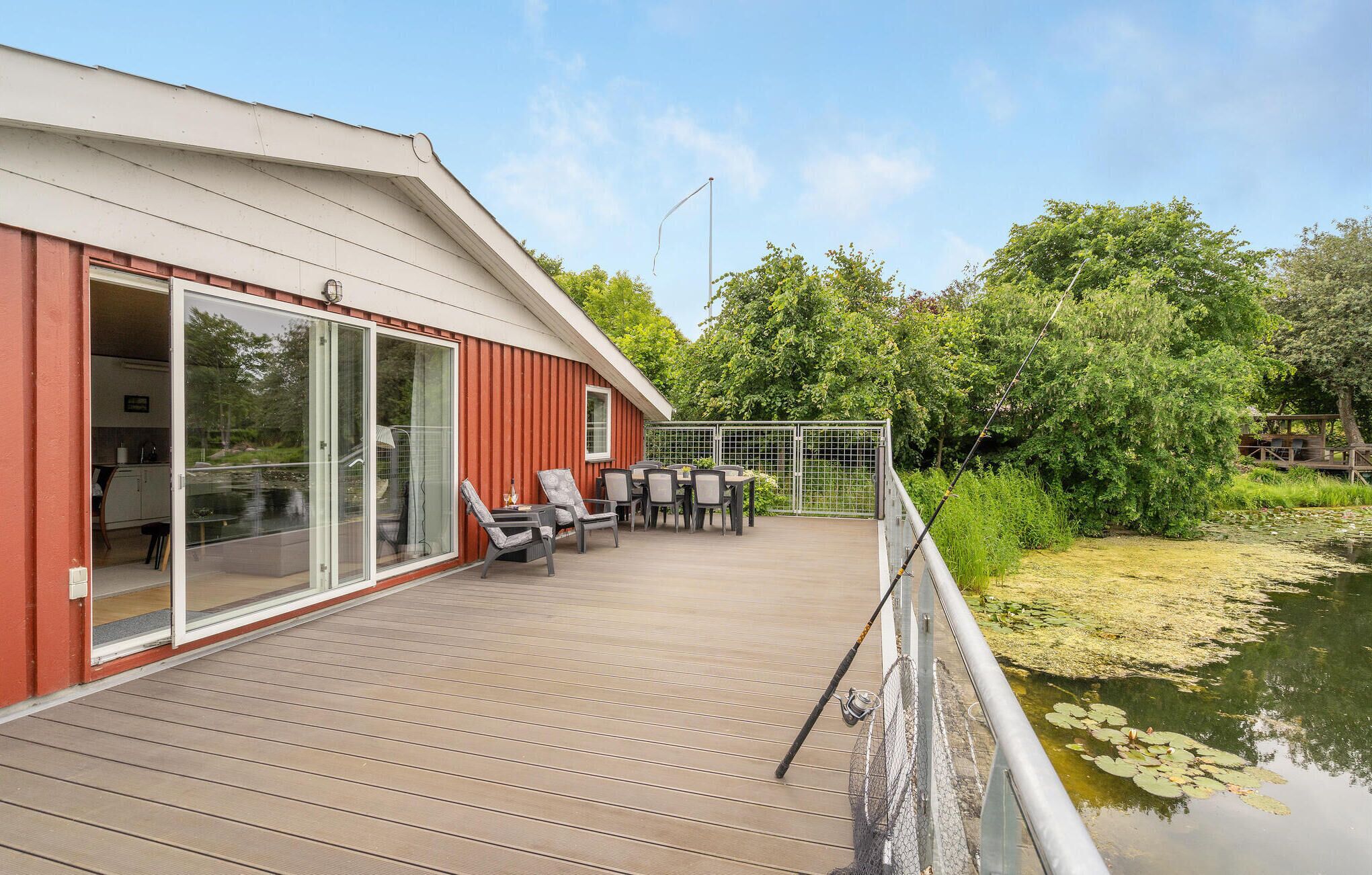 A wooden deck with a glass door leading to a room, a table with chairs, and a view of a pond with lily pads.