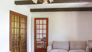 Una habitación con un sofá color crema, una puerta de madera con paneles de vidrio y una pared blanca.