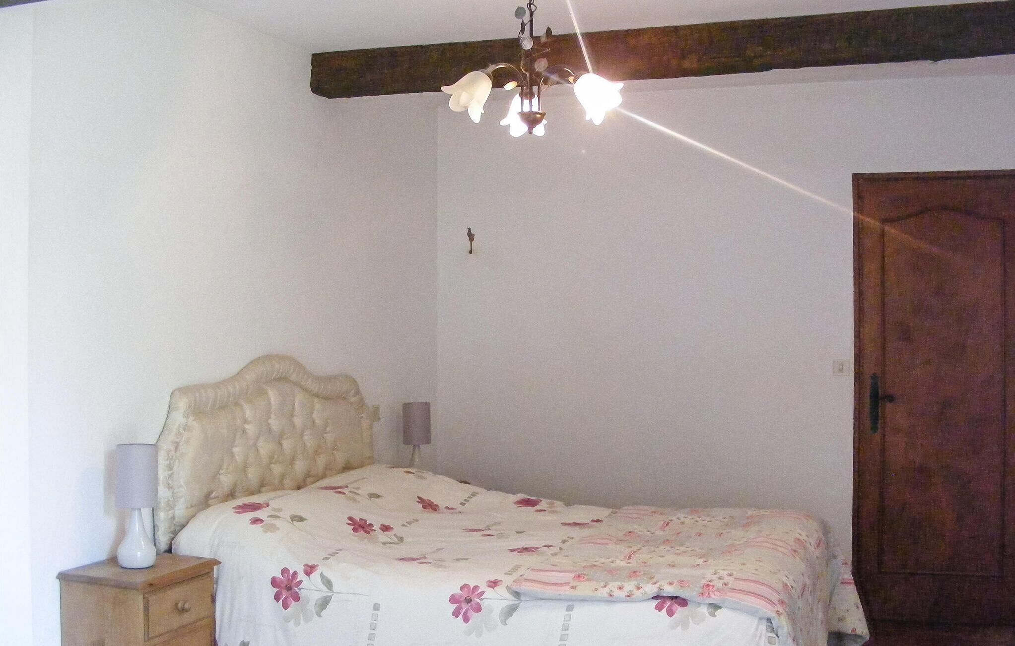 Camera da letto con un letto, un comodino, una lampada, una porta in legno e un lampadario.