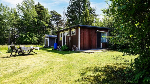 A small, single-story wooden cabin with a porch, a table with chairs, and a blue barrel in the yard. - 2 bedroom lovely home in Slite (Slite)