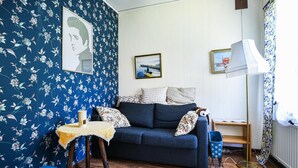 A cozy room with a blue floral wallpaper, a dark blue sofa, a small table with a lace tablecloth, and a framed picture on the wall. - 2 bedroom lovely home in Slite (Slite)