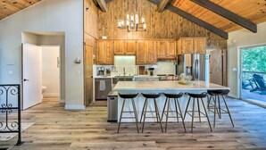 A spacious kitchen with wooden cabinets, a large island with bar stools, and a hanging light fixture. - Pine Mountain Cabin w/ Hot Tub, 2 Mins to Marina! (Groveland)