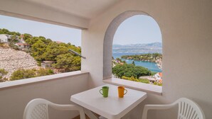 Un balcon avec une table et des chaises, donnant sur un paysage côtier avec des maisons et des arbres.