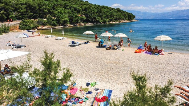 Une plage avec une eau cristalline, des parasols et des gens.