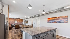 A modern kitchen with granite countertops, a central island, and a dining area with a brick wall and wooden flooring.