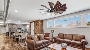 A modern living room with a brown leather sofa, a wooden coffee table, and a large window with a view of trees.