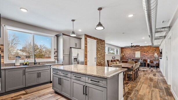 A modern kitchen with grey cabinets, a large island, and a brick accent wall.