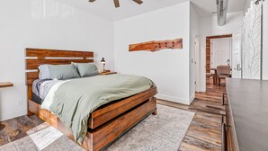 A bedroom with a wooden bed, a ceiling fan, a wall-mounted light, and a wooden wall art piece.