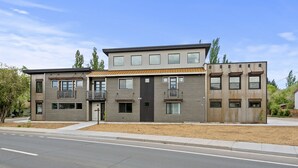 A modern two-story residential building with a flat roof, large windows, and a balcony on the second floor.