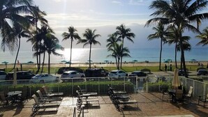 A poolside area with lounge chairs and umbrellas, palm trees, and a view of the beach and ocean. - THE ONE! NEWLY RENOVATED GROUNDFLOOR BEACH/OCEAN FRONT CONDO with private deck! (Deerfield Beach)
