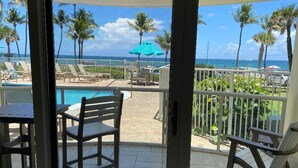 A balcony with a view of a pool and palm trees, a table, and chairs. - THE ONE! NEWLY RENOVATED GROUNDFLOOR BEACH/OCEAN FRONT CONDO with private deck! (Deerfield Beach)