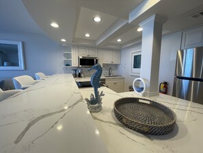 A modern kitchen with white cabinetry, a large island with a woven basket, and a stainless steel refrigerator.
