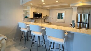 A modern kitchen with white cabinetry, a marble countertop, and three bar stools. - THE ONE! NEWLY RENOVATED GROUNDFLOOR BEACH/OCEAN FRONT CONDO with private deck! (Deerfield Beach)