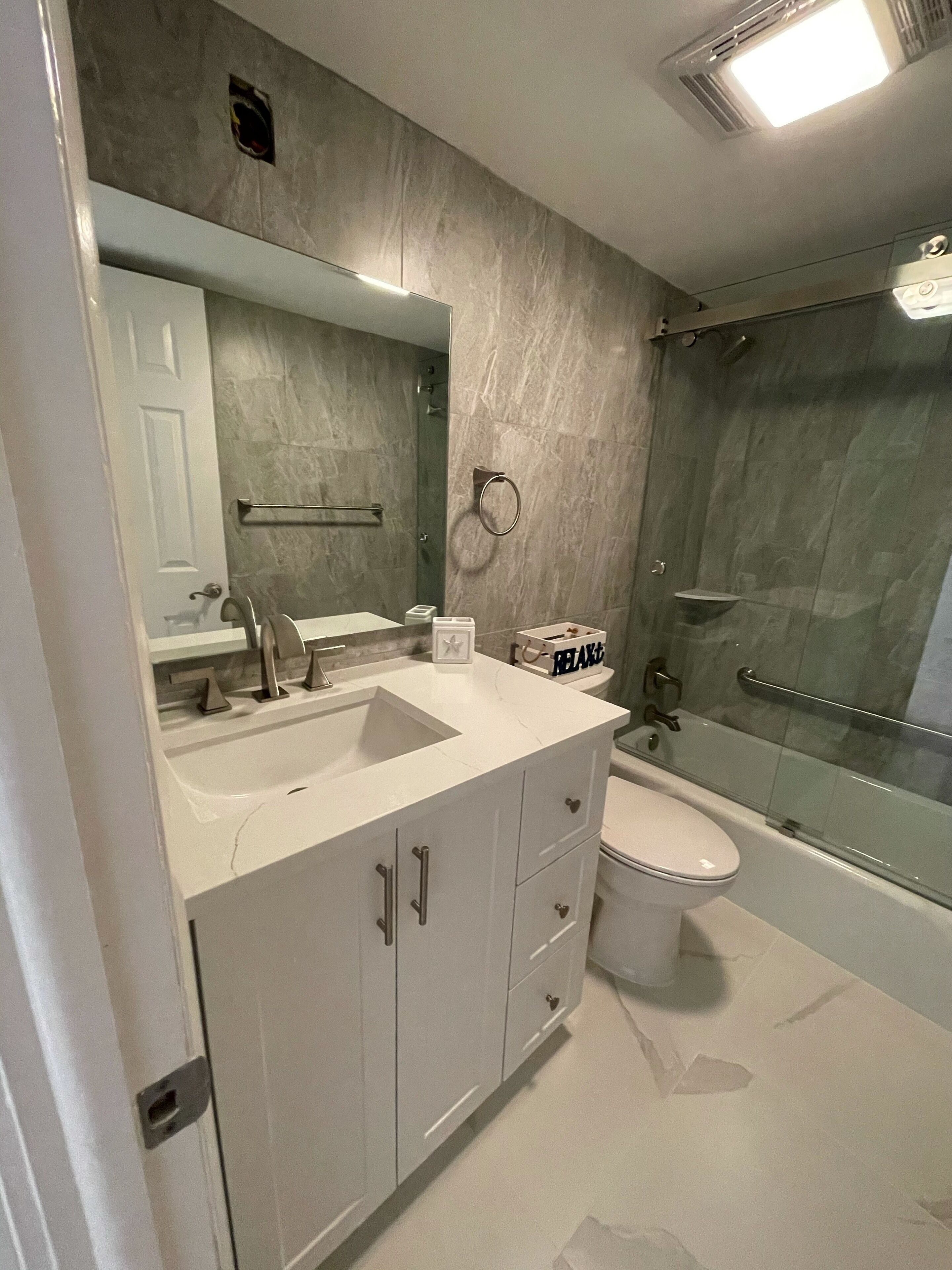 Een moderne badkamer met een wit wastafelmeubel, een grote spiegel, een toilet en een douchecabine met glazen wanden.