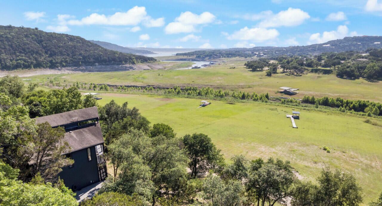 A large, open grassy area with a few scattered trees, a small building, and a distant view of a body of water.
