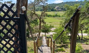 Eine Holztreppe führt zu einer grünen Wiese mit Bäumen und weiter Blick auf ein Haus.