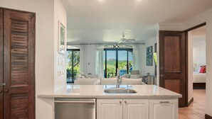 A kitchen with a built-in dishwasher, a sink, and a view of a living area with a sofa and a dining table.