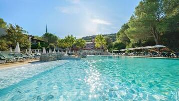 Une piscine aux eaux cristallines, bordée de chaises longues et d’ombrelles, et entourée d’arbres et d’immeubles.