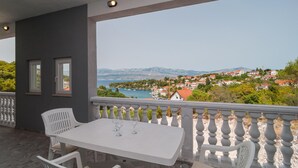 Un balcón con mesa y sillas, con vista a un pueblo costero con casas y al mar.