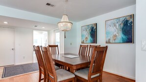 A dining area with a wooden table and chairs, a chandelier, and two abstract paintings on the wall. - Awesome End Unit Spinnaker! 3 BR Close to Beach w/Amenity access included! Pet Friendly! (Seabrook Island)