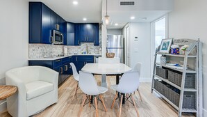 Een moderne keuken met donkerblauwe kastjes, een witte eettafel en witte stoelen.