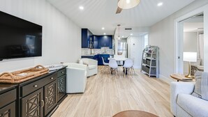Een moderne woonkamer met een flatscreen-tv, een plafondventilator en een eethoek met een tafel en stoelen.