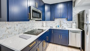 Een moderne keuken met donkerblauwe kastjes, roestvrijstalen apparatuur en een wit marmeren aanrecht.