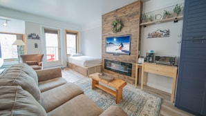 A modern living room with a sofa, a TV mounted on a wooden wall, a fireplace, and a small coffee table.