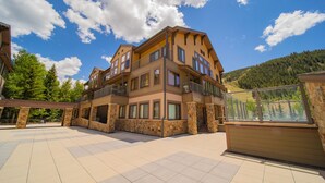 A multi-story building with a balcony, stone pillars, and a view of a forested hillside.