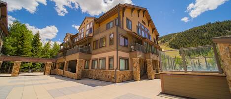 A multi-story building with a balcony, stone pillars, and a view of a forested hillside.