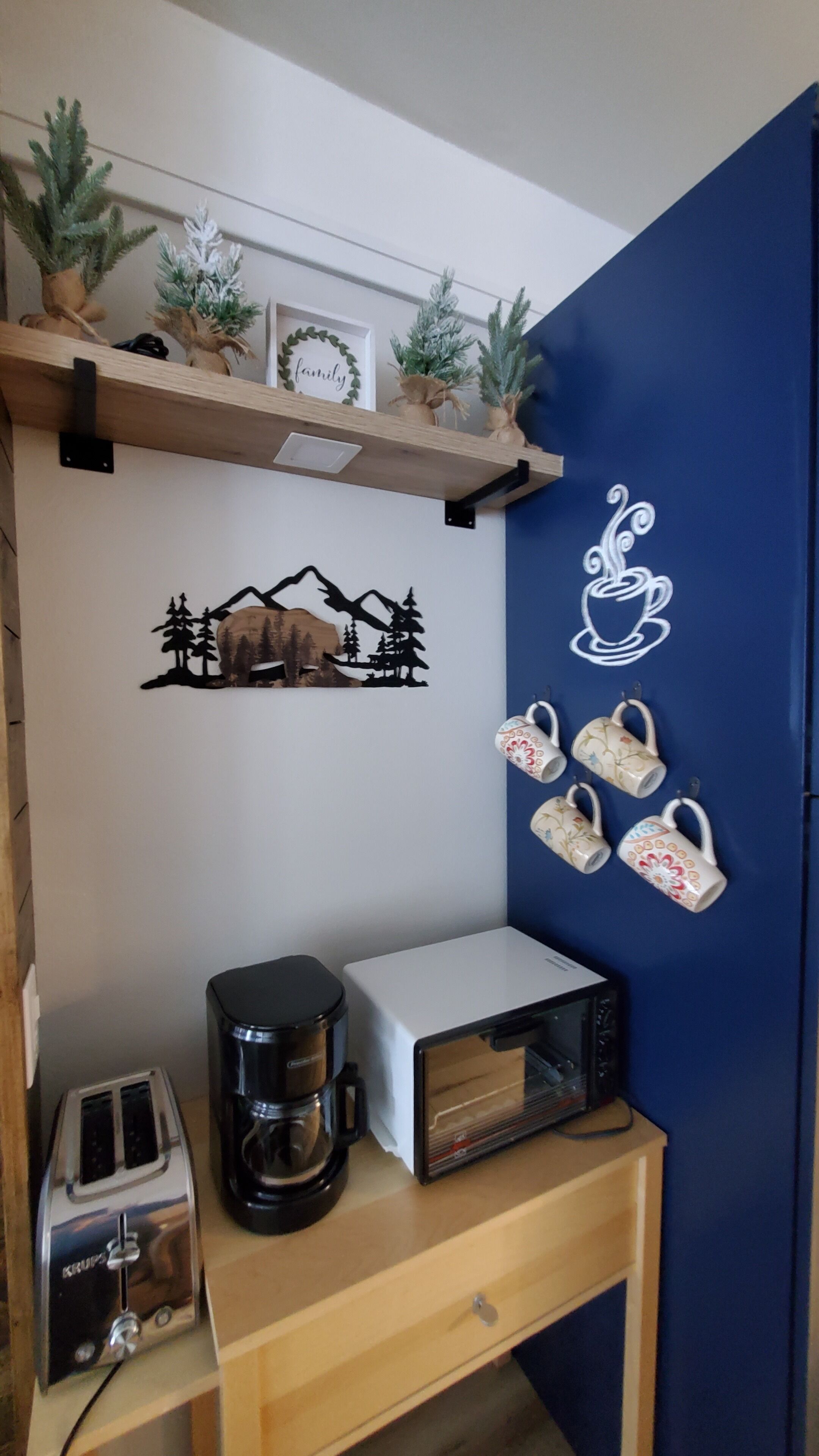 A kitchen with a wooden shelf holding decorative items, a coffee maker, a toaster, and a microwave on a wooden table.