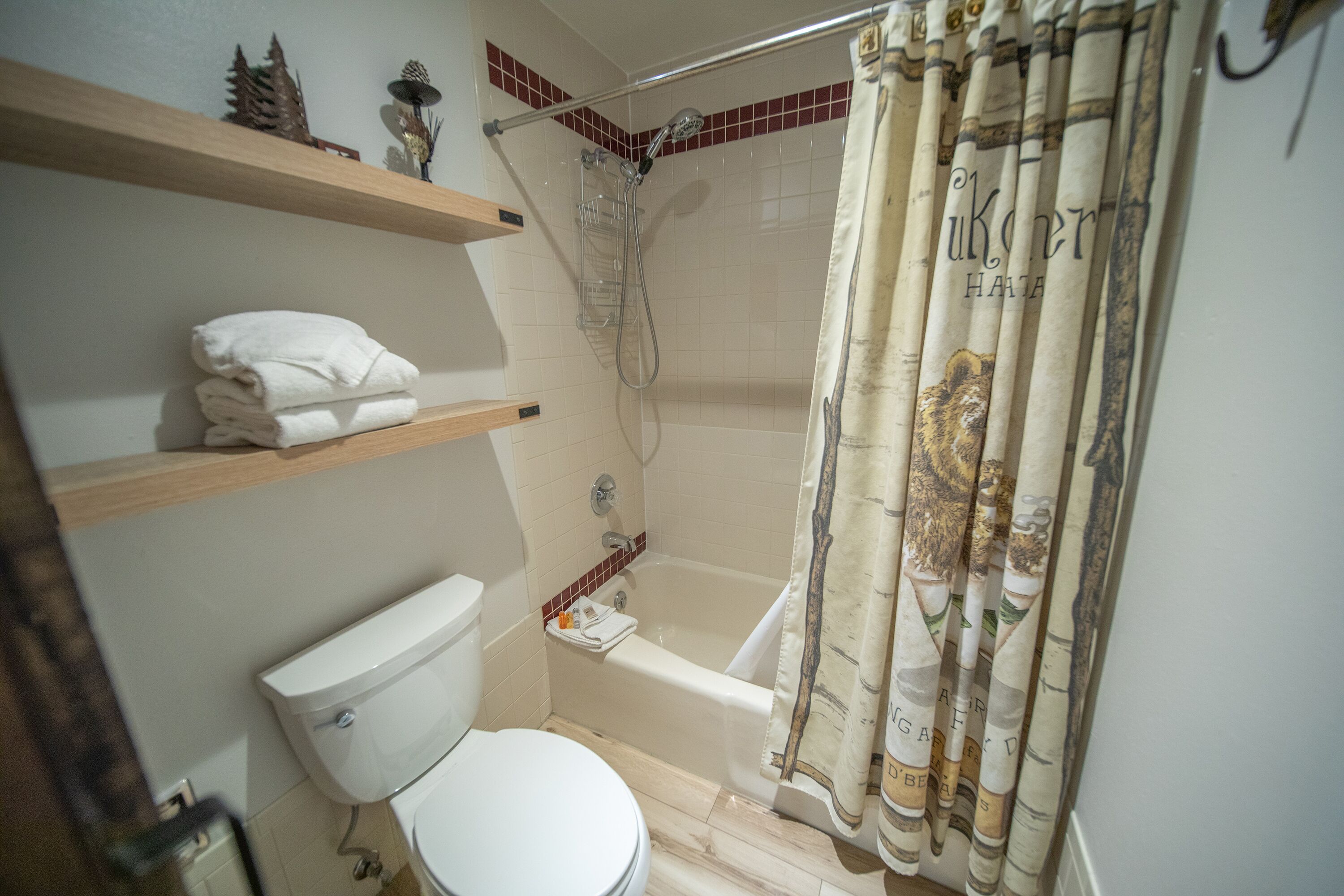 A bathroom with a toilet, a shower, and a bathtub. There are shelves above the toilet and a shower curtain with a tiger design.