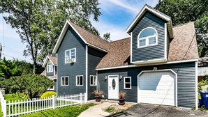 Een tweelaags huis met garage, een witte picket fence en een verzorgd gazon.