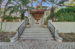 A stone staircase leading to a wooden pergola with a wreath at the top, surrounded by greenery.