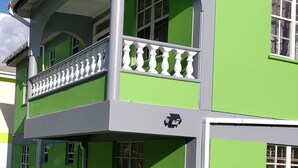 En toetagers bygning med en grøn facade, hvide vinduesrammer og en balkon med hvide gelændere.