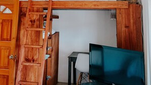 Un letto a castello con scala in legno, una scrivania con sedia e un televisore.