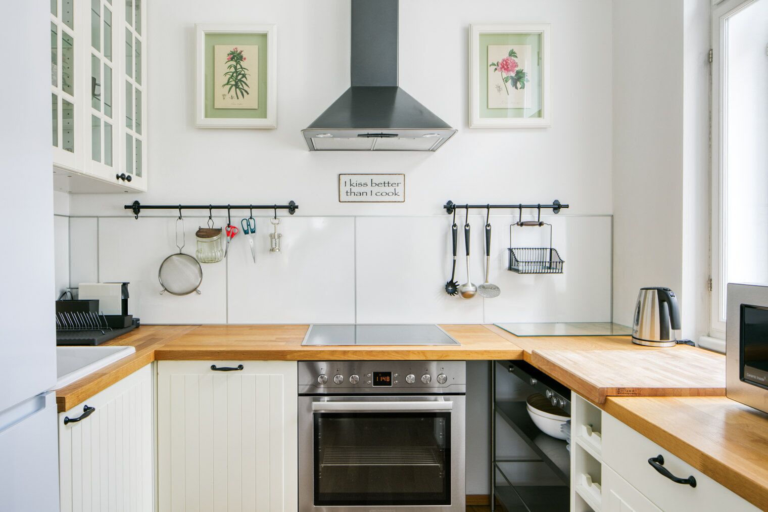 Una cocina con armarios blancos, una campana extractora de acero inoxidable y un panel digital del horno.
