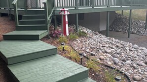 A building with a green staircase leading to a deck, a red and white lighthouse, and a stone wall. - Lake Huron Cottage (East Tawas)