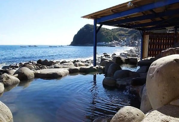 Enjoy a tranquil beach experience with a shaded gazebo overlooking the calm sea and rocky shoreline.