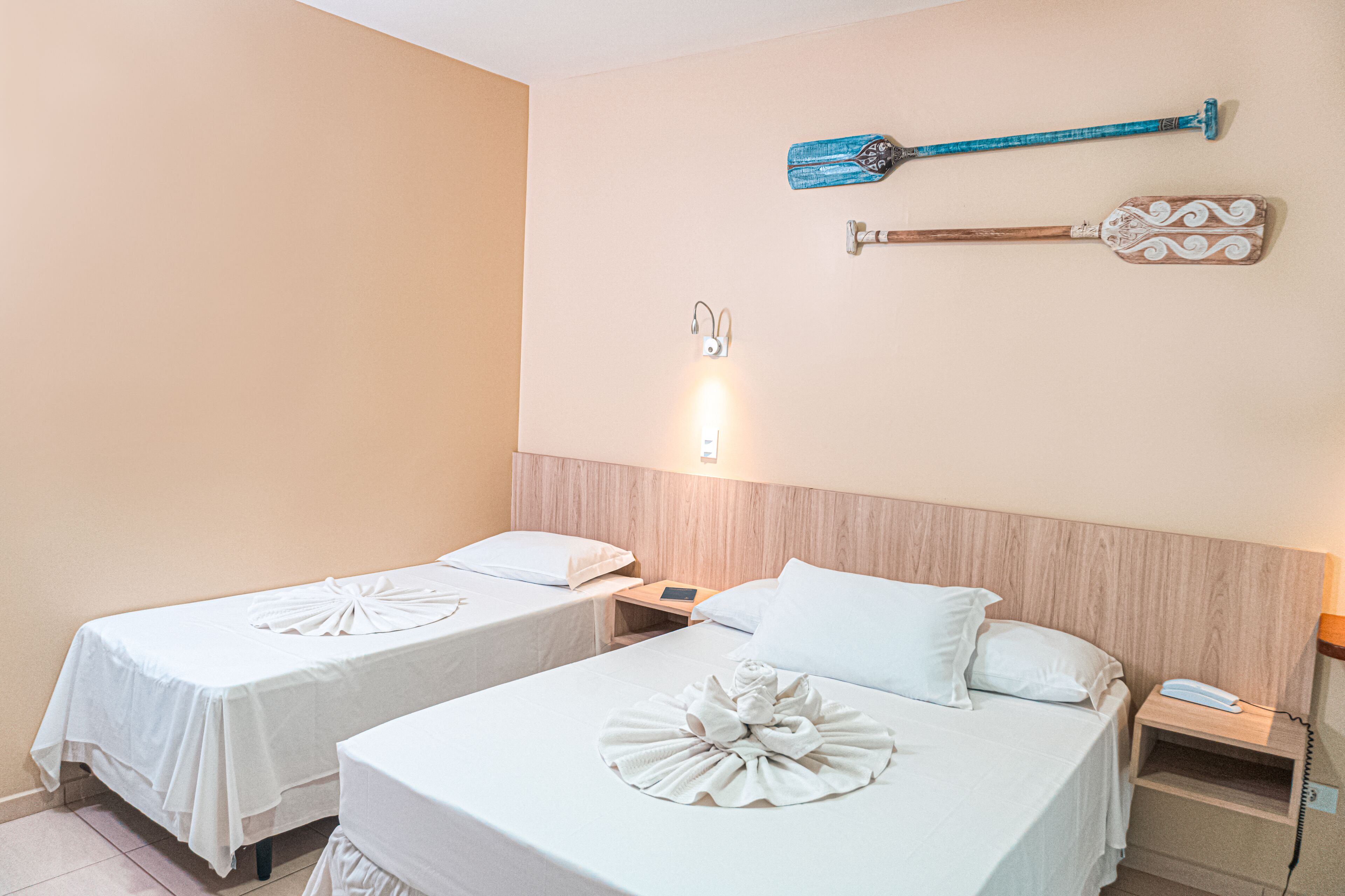 A hotel room with two beds, a wooden headboard, a wall-mounted telephone, and a wall-mounted light fixture.